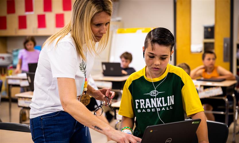 A teacher helps a student as they use a Chromebook